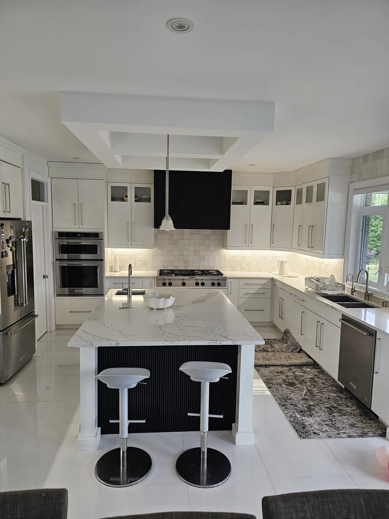 White kitchen with a marble island, black range hood and glass front uppers